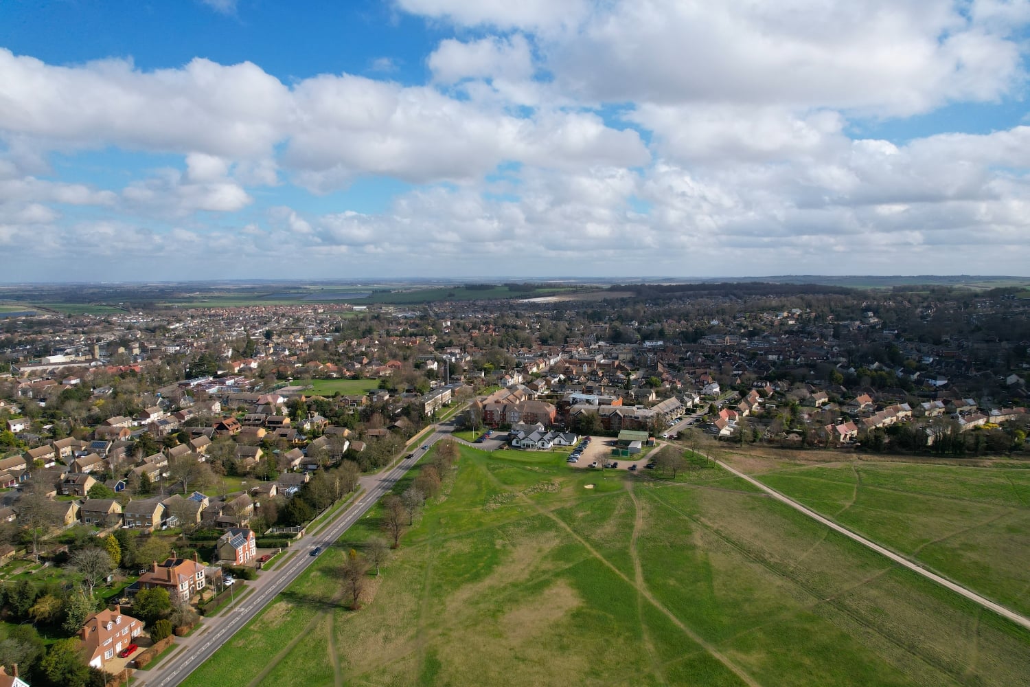 a large green field with buildings and trees around it