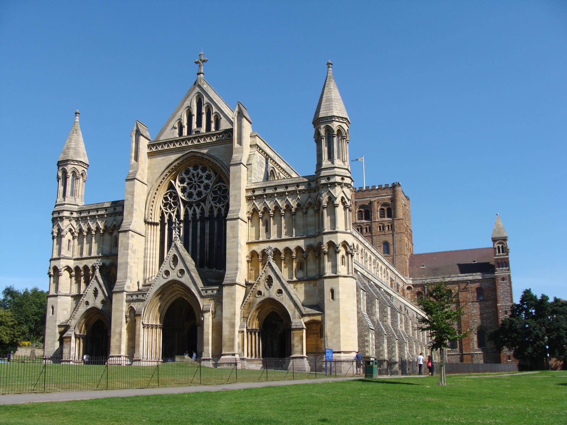 a large building with a fence around it with St Albans Cathedral in the background