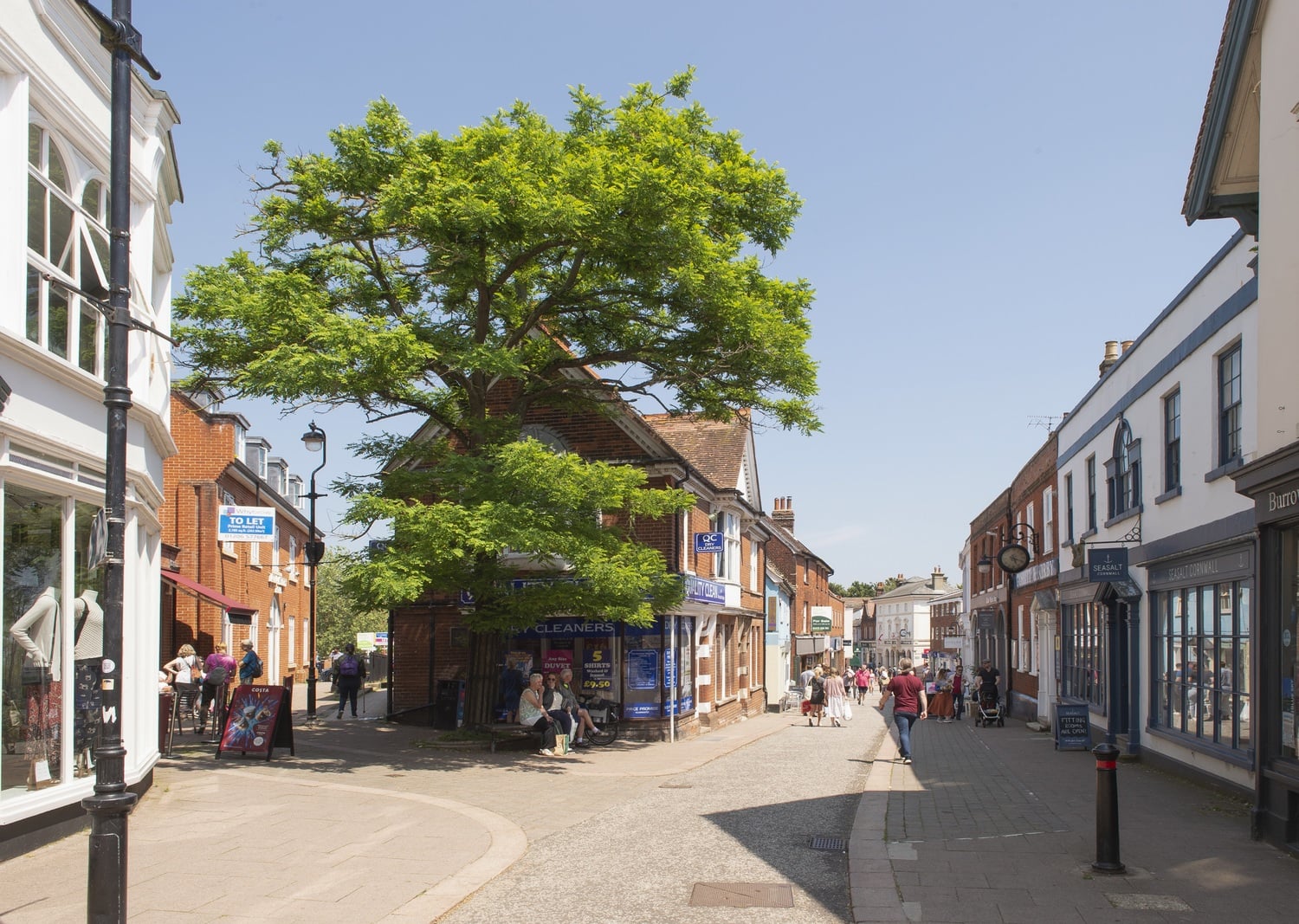 A narrow street with shops on both sides and people walking along it.