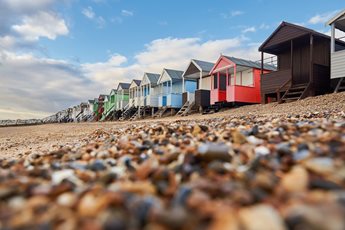 A row of multicoloured beach huts on a pebble shoreline.