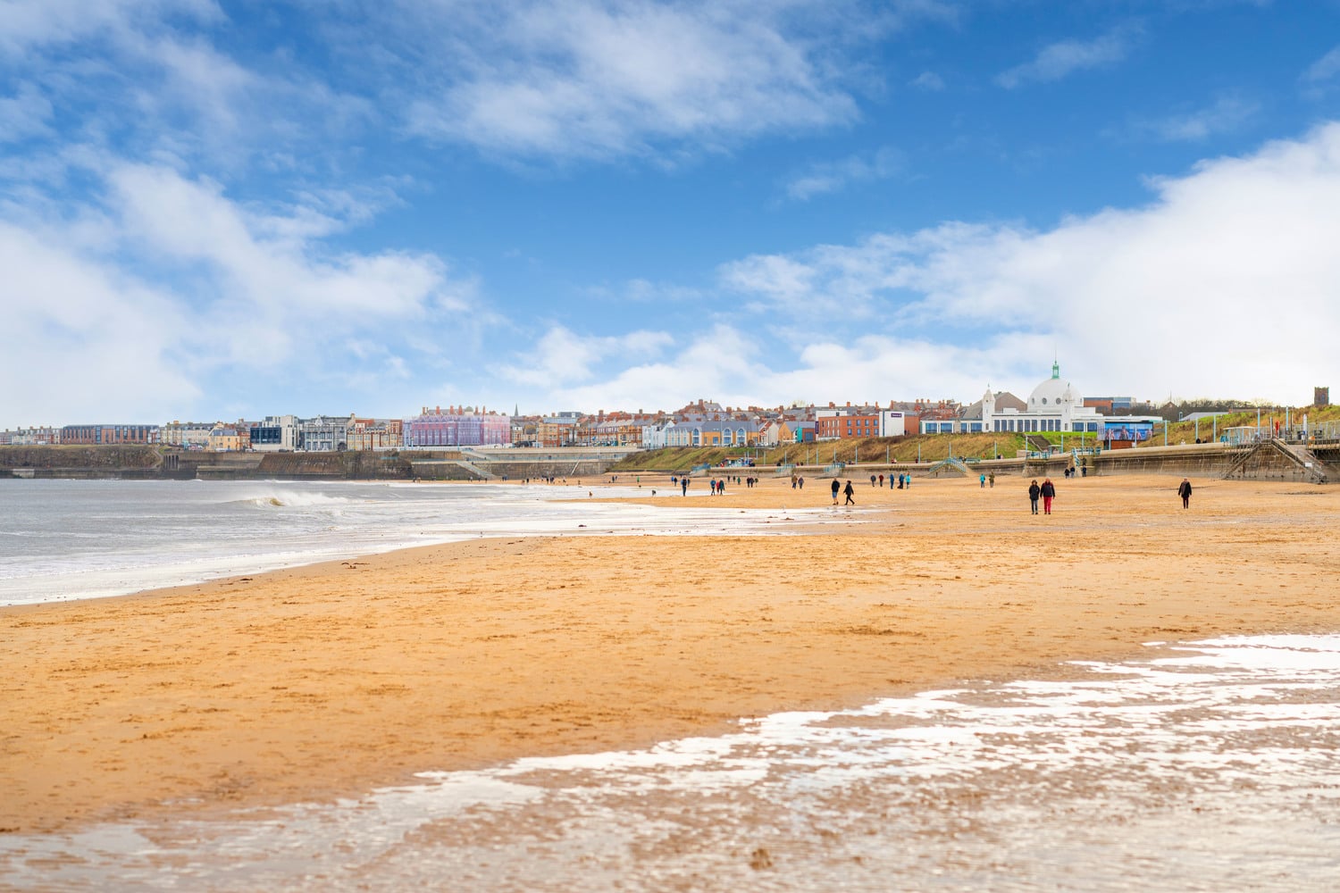 Whitley Bay beach with people walking along it and the town buildings in background.