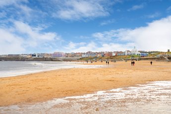 Whitley Bay beach with people walking along it and the town buildings in background.