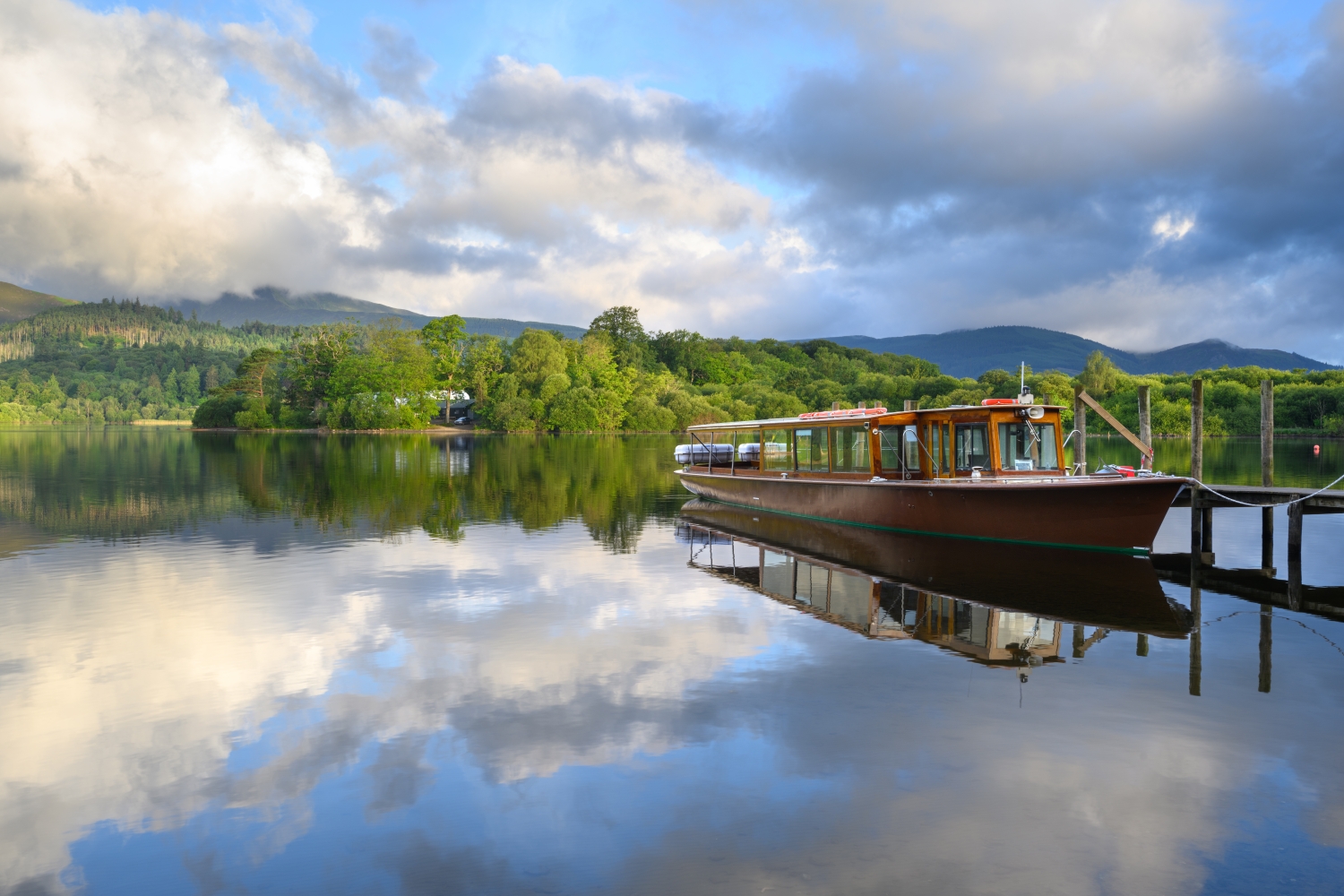 Cruise boat moored next to jetty on calm waters at Derwentwater, Lake District.
