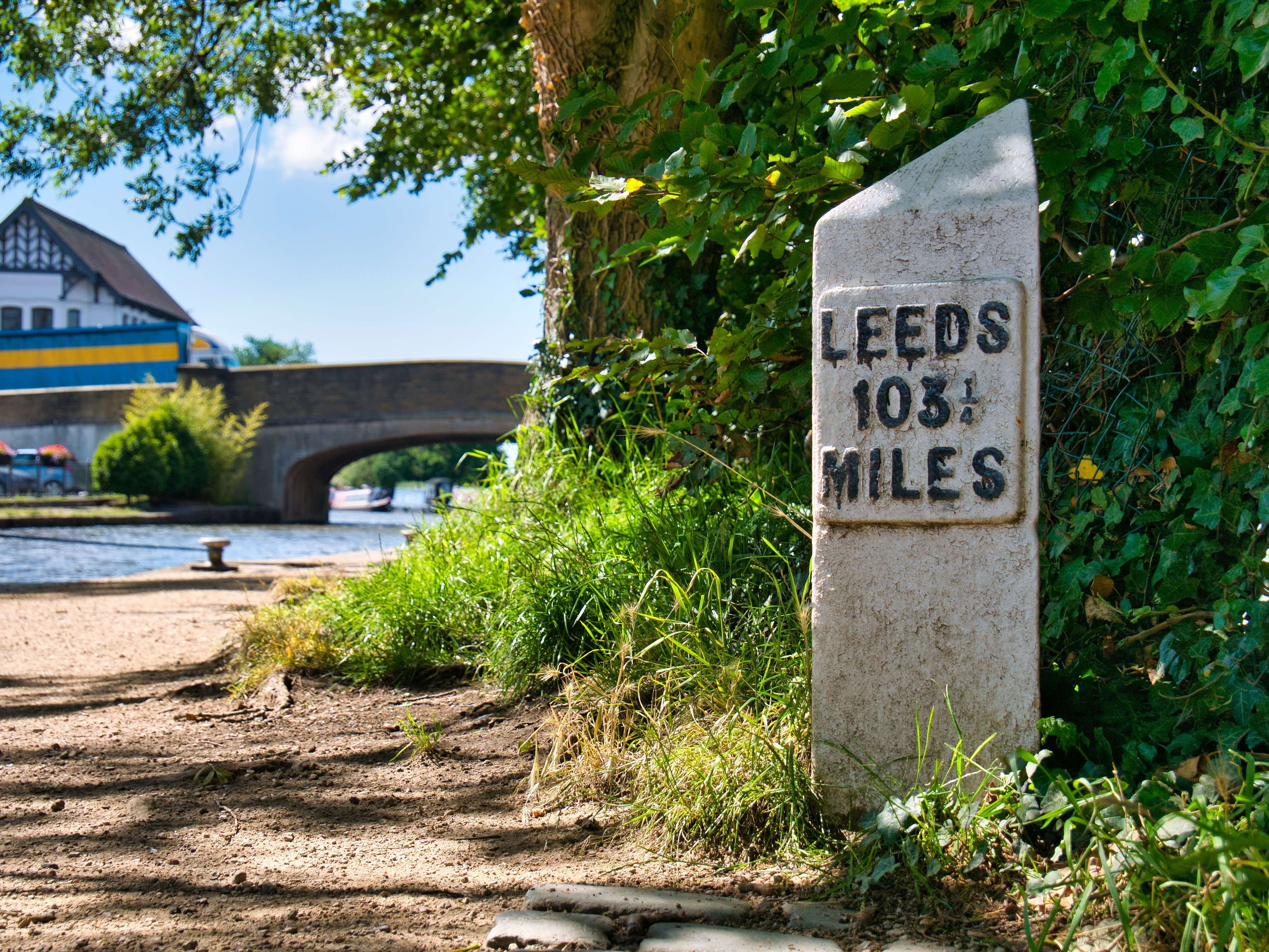 Focus on a distance marker in Burscough on the Leeds to Liverpool Canal in Lancashire in the UK. Burscough Bridge appears in the background.