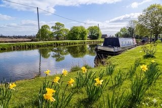 A moored up canal boat on the Leeds Liverpool Canal running through Burscough on a sunny summer day.