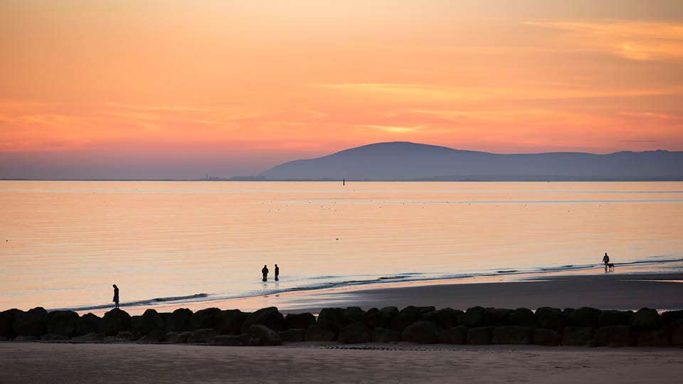 a couple of people walking on a beach with a body of water in the background