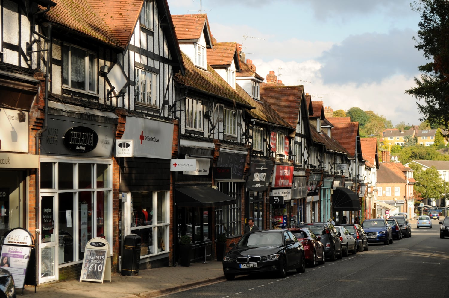 A main road with cars, lined with shops and Tudor-style buildings.