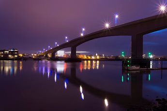 Itchen Bridge over still water in Southampton at night, with light reflected on the water.