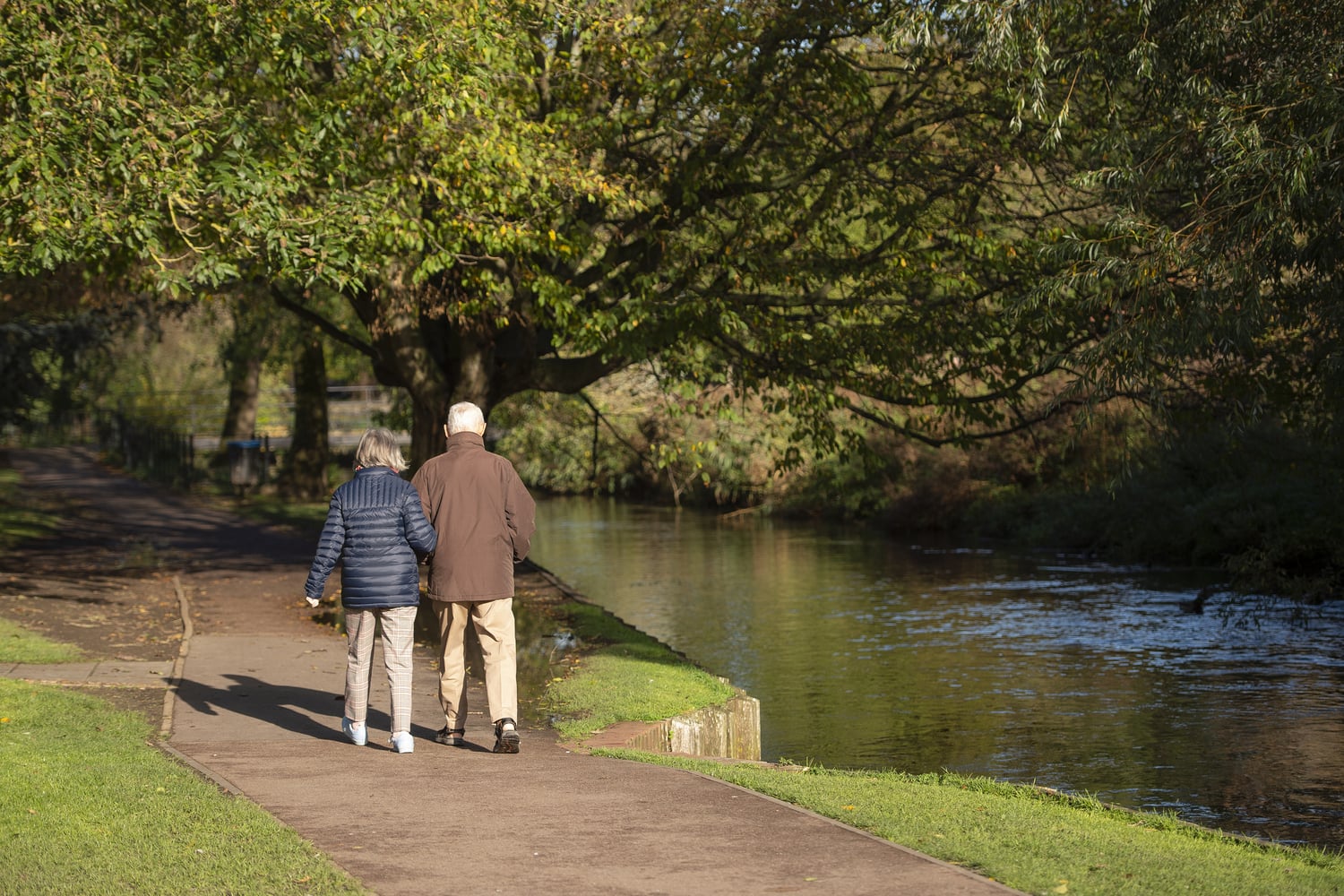 A man and woman walking on a path through Westgate Gardens next to the River Stour.