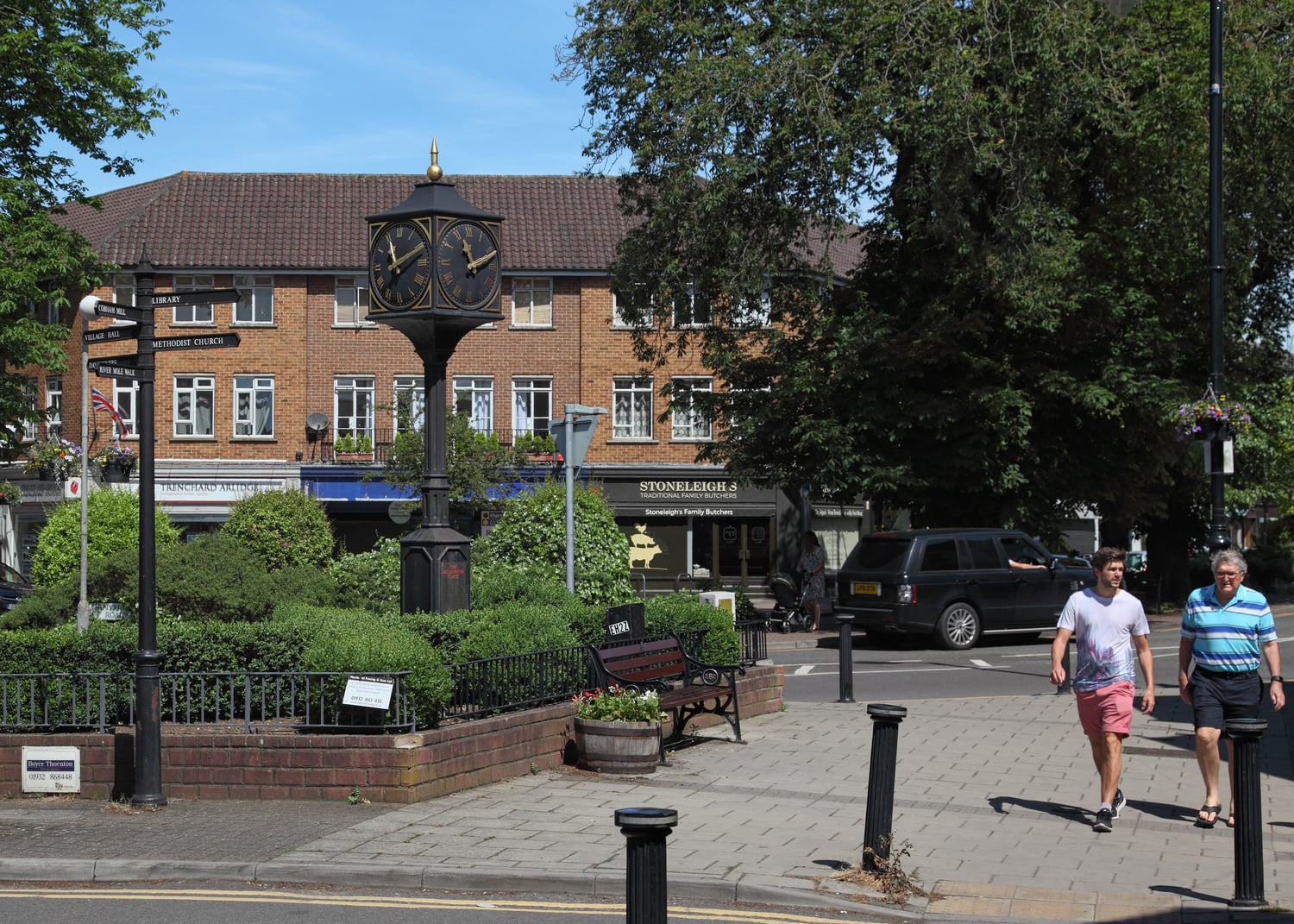 A couple of people walk down the high street next to the Millennium Clock, Cobham.