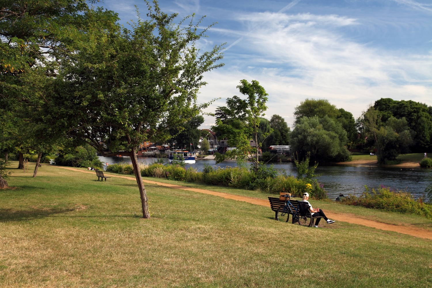 A senior woman sits on a bench by the River Thames.