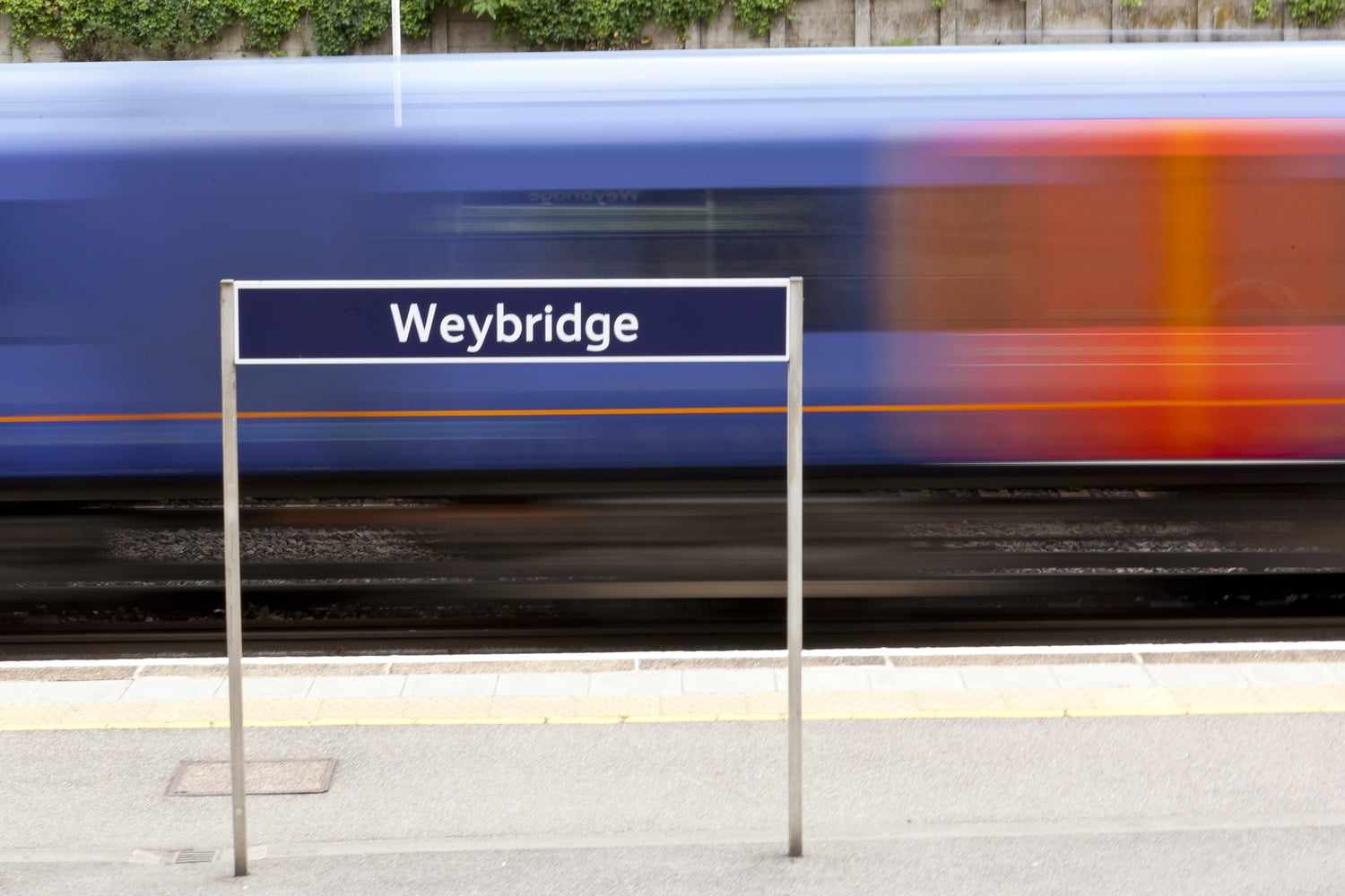 A train on the railway tracks passing through Weybridge train station.