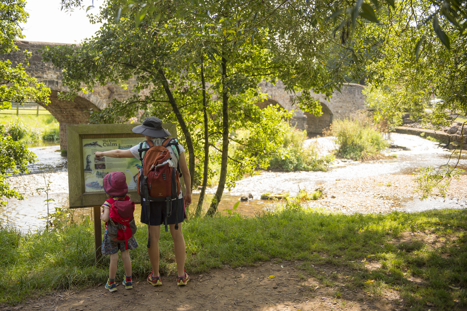 A senior adult and child looking at a map sign next to the River Culm.
