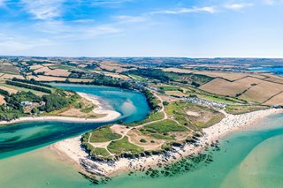 An aerial view of one of Devon’s many coasts, with fields and rolling green hills in the surroundings.