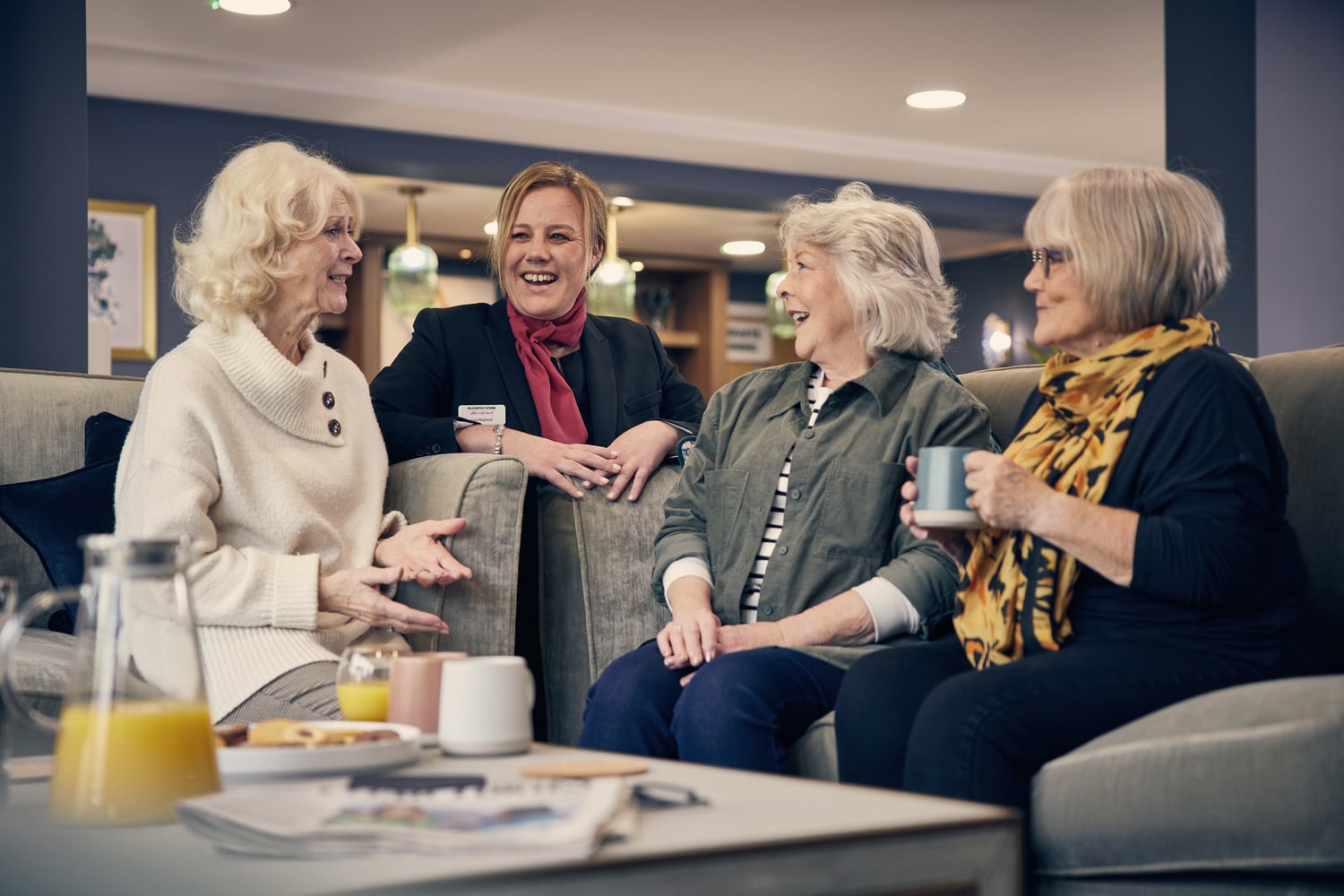 Three retired ladies and a McCarthy & Stone retirement development manager chatting and laughing during a coffee morning.