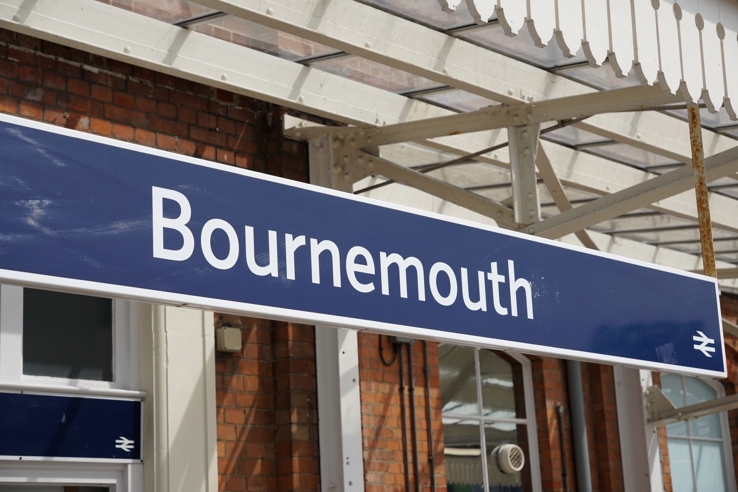A blue 'Bournemouth' railway station sign hanging from a platform canopy.