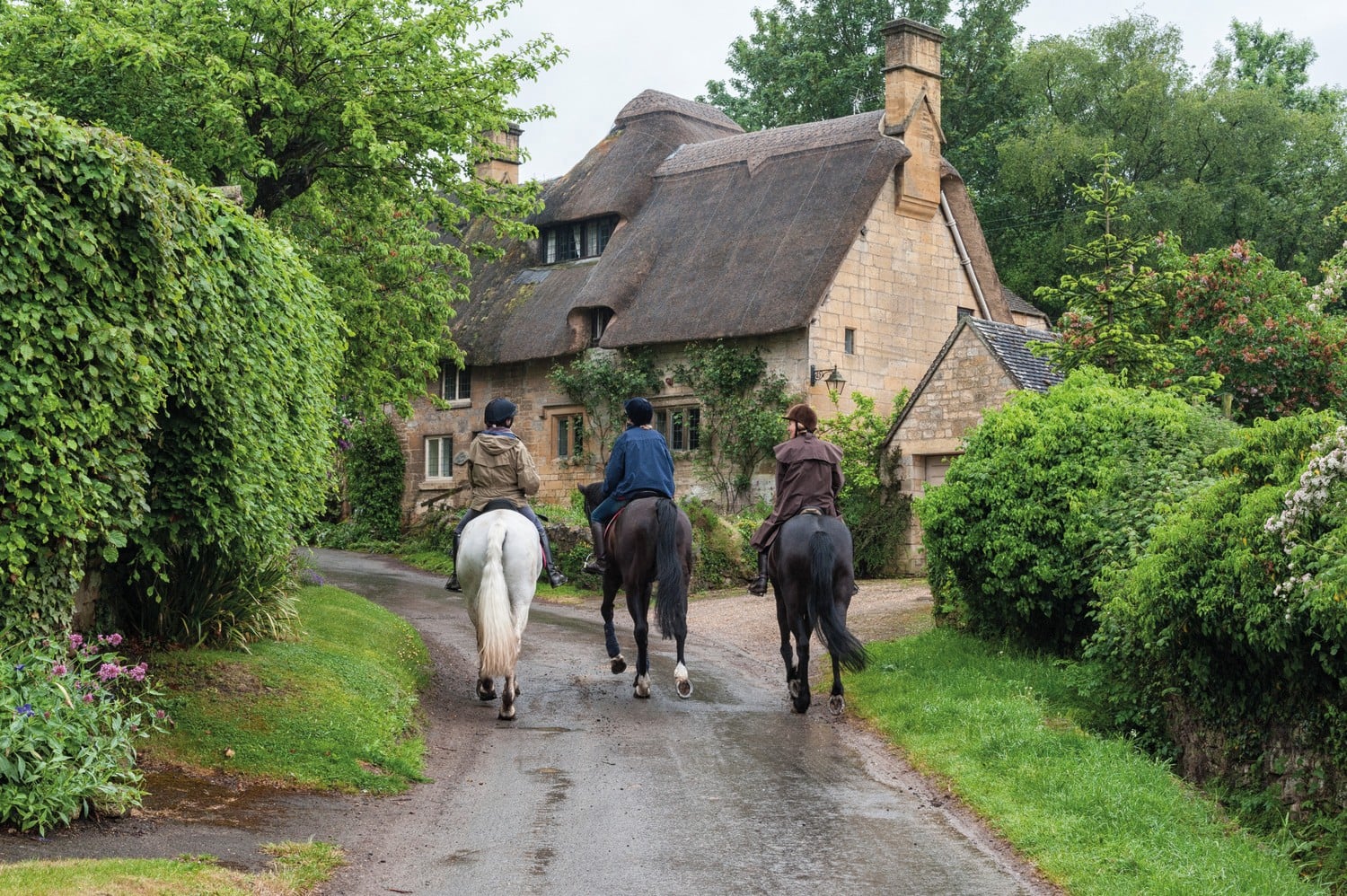 Three people riding horses along a country lane in Stow-on-the-Wold.