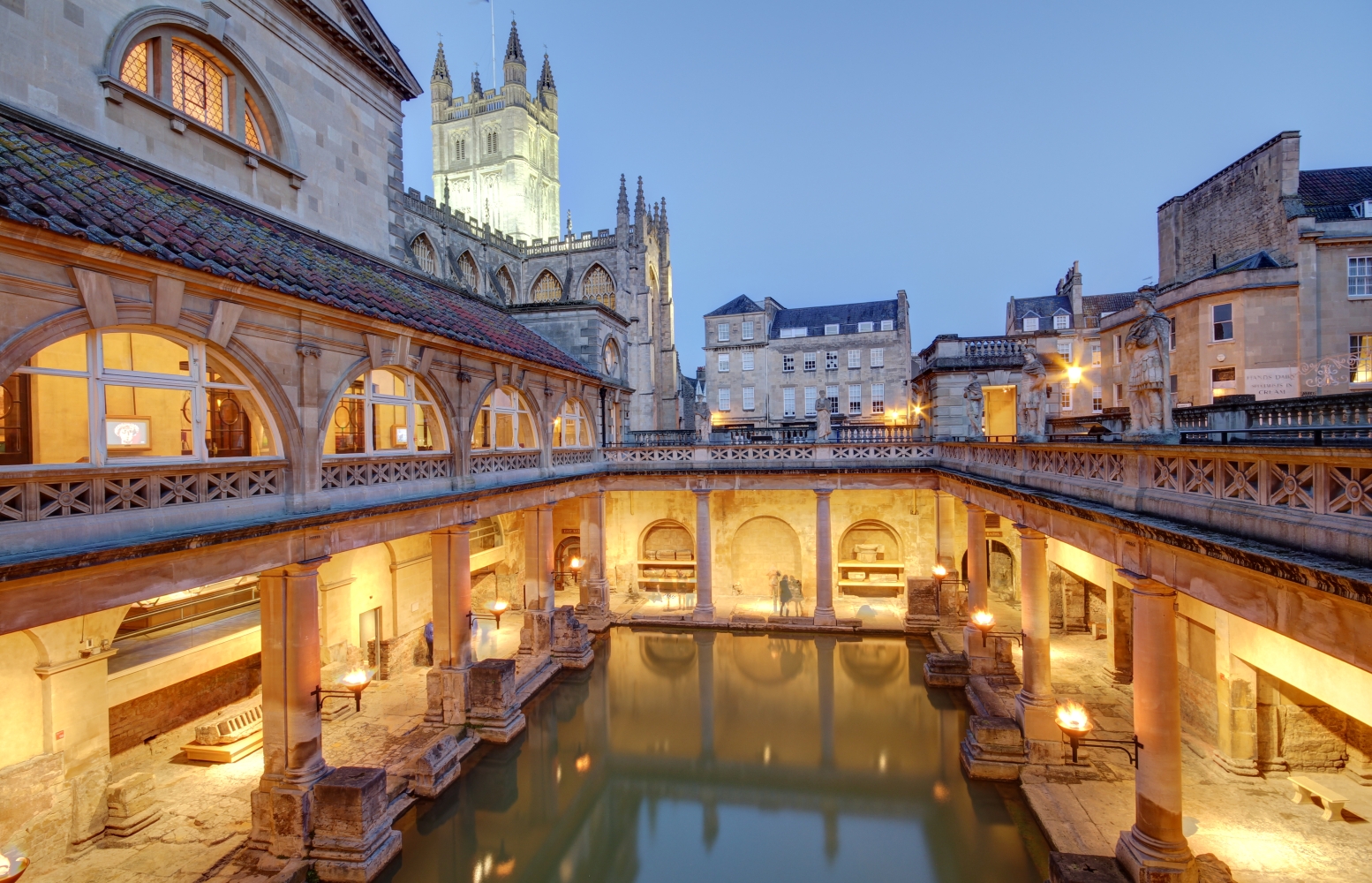 The Roman Baths in Bath at Dusk with Bath Abbey in background lit up.