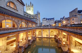 The Roman Baths in Bath at Dusk with Bath Abbey in background lit up.
