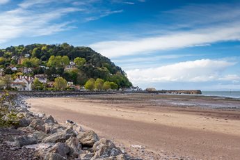 a beach with rocks and trees and Minehead harbour in the distance