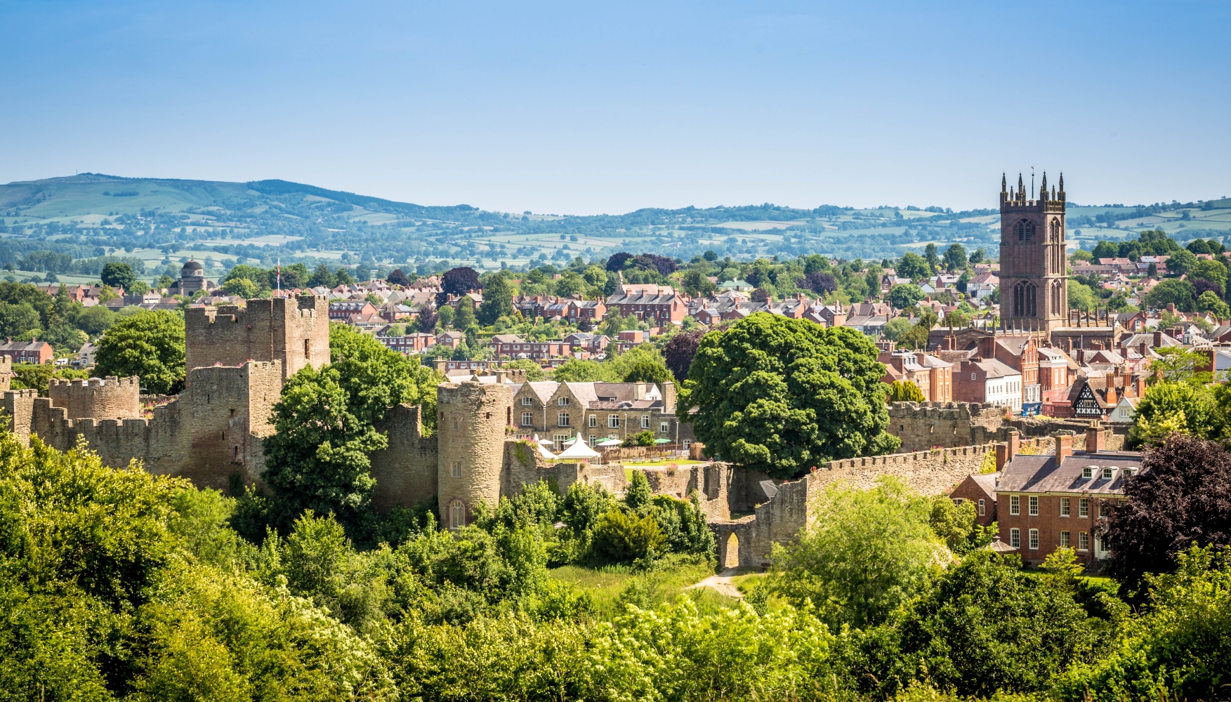 An aerial view of Ludlow Castle and surround town buildings and rolling hills in Shropshire.