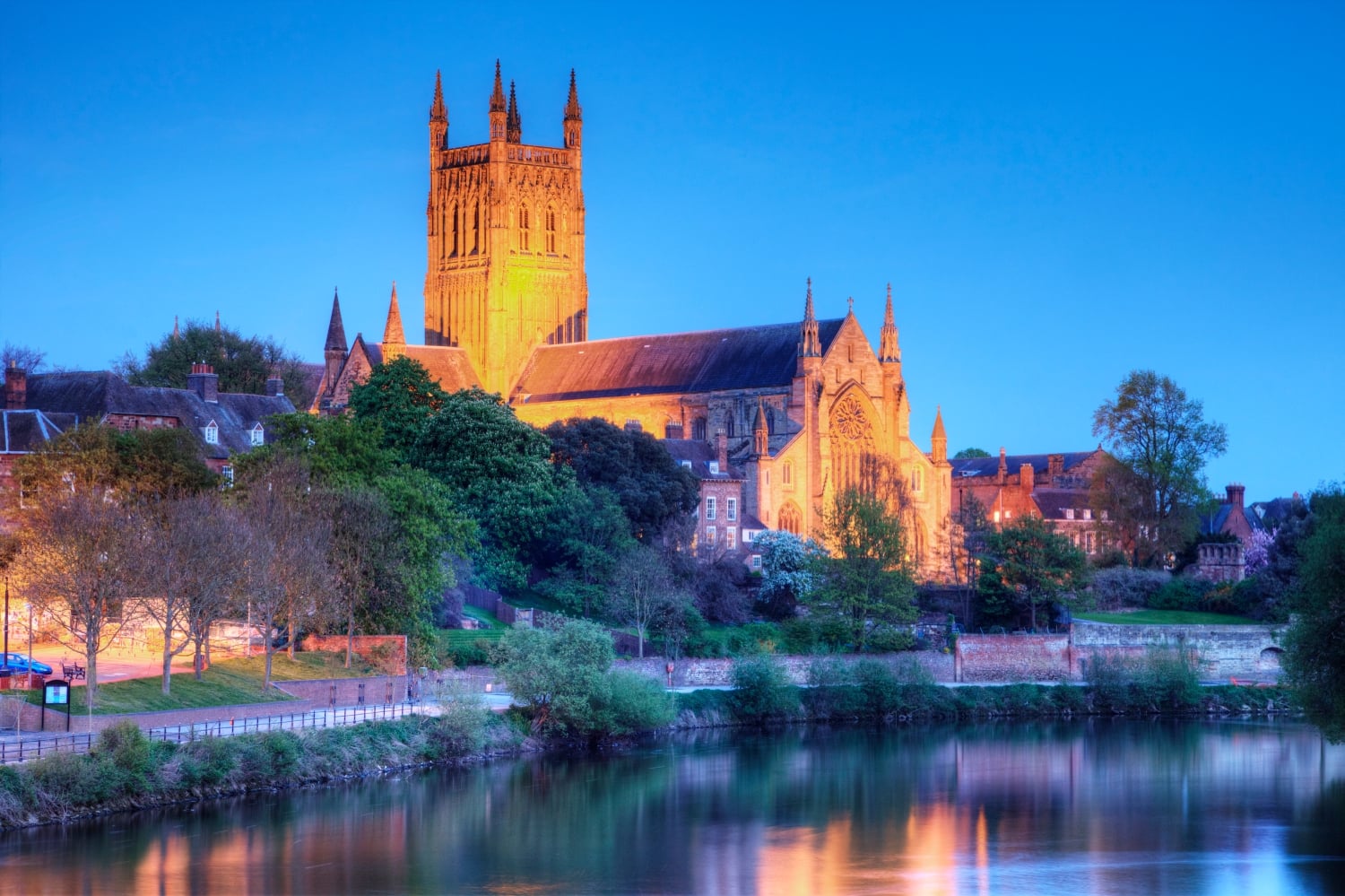 Worcester Cathedral floodlit next to the River Severn at dusk.