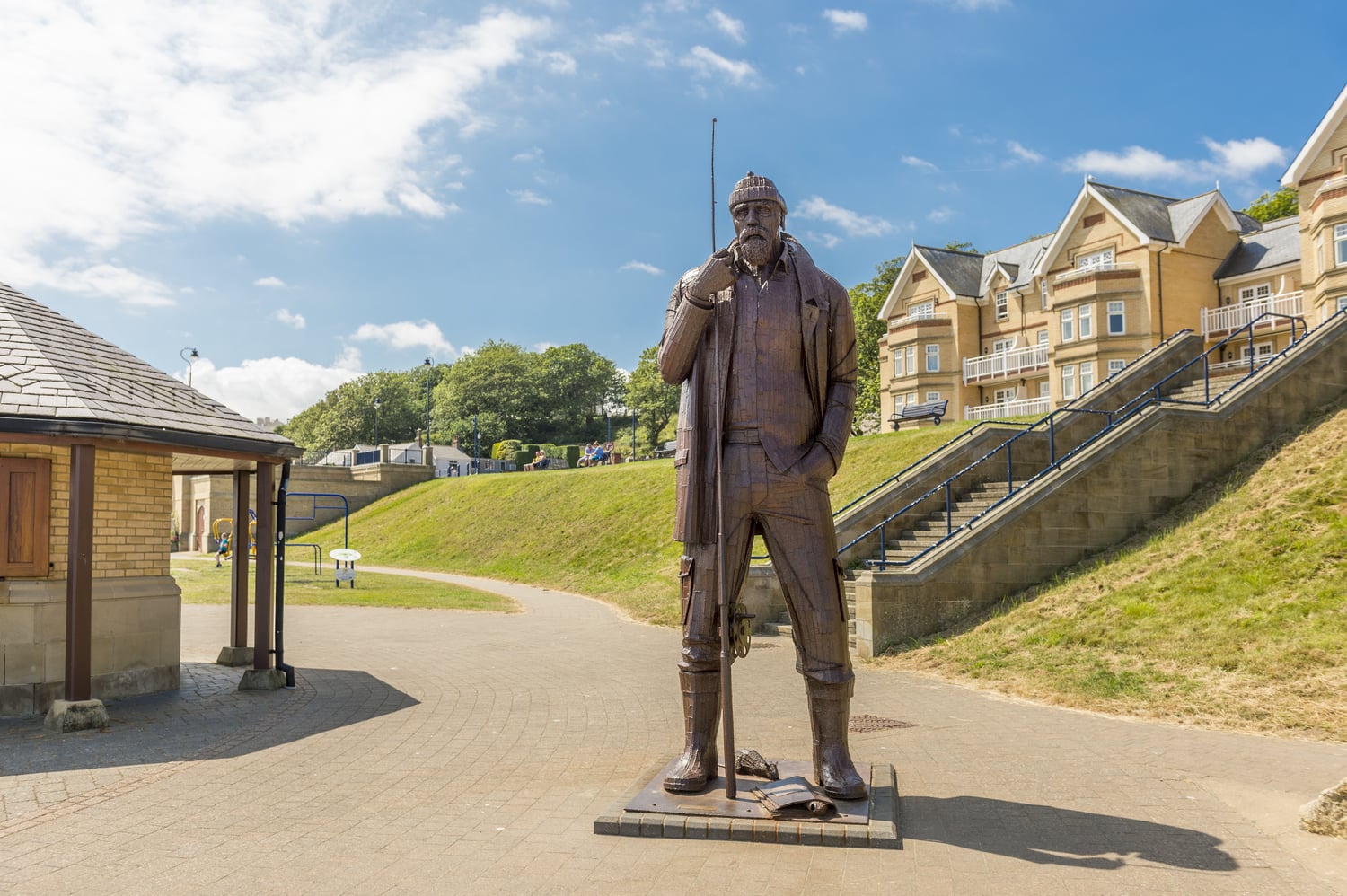 A 12-foot tall weathered steel sculpture called "A High Tide in Short Wellies" by sculptor Ray Lonsdale depicts a fisherman holding a fishing rod.