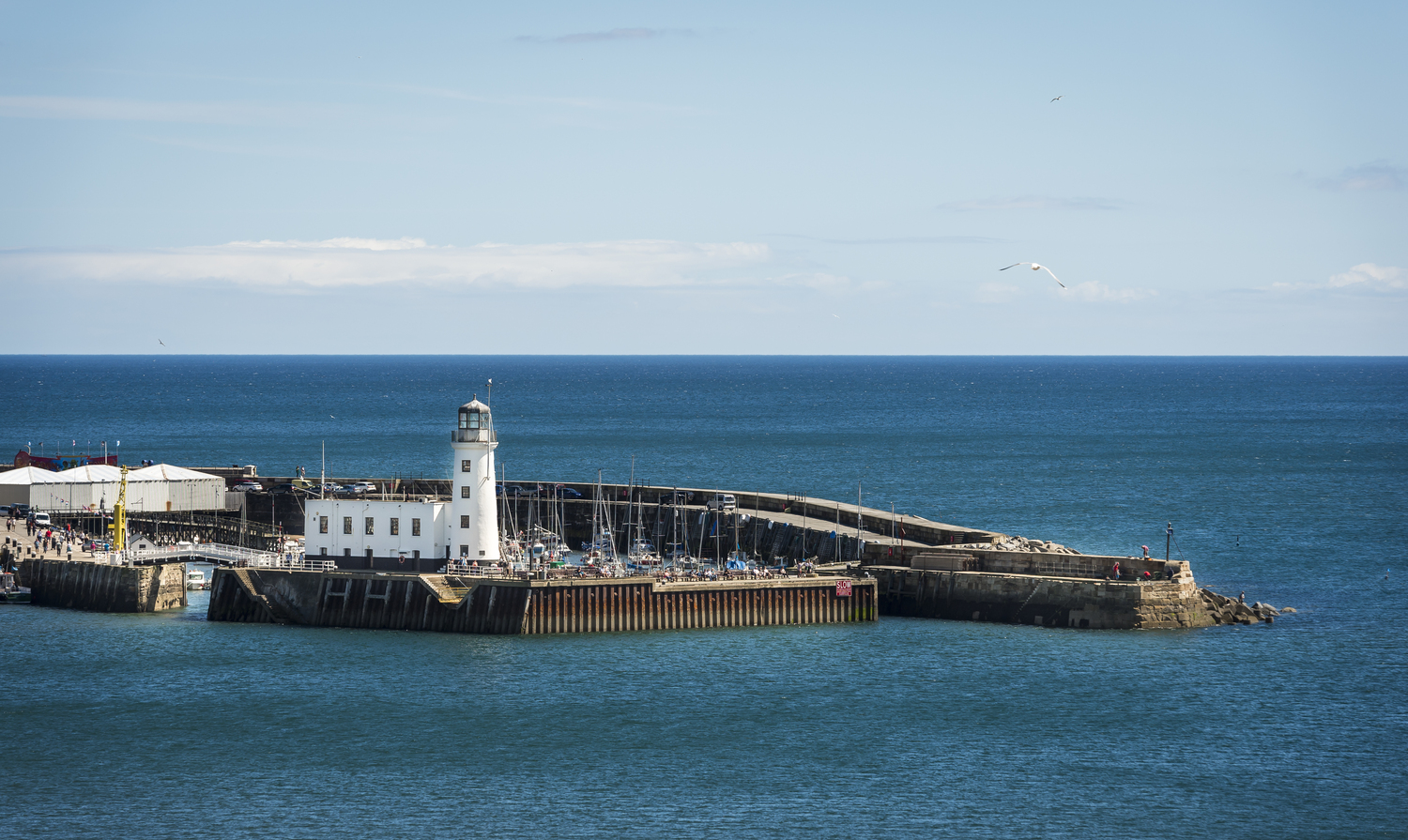 A pier with a white lighthouse surrounded by water.