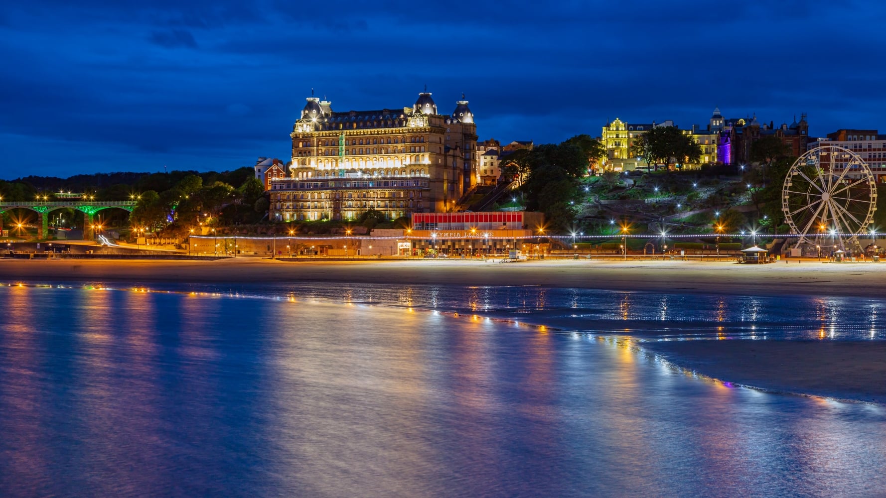 Scarborough South Bay at night with seafront buildings and amusements in lights.