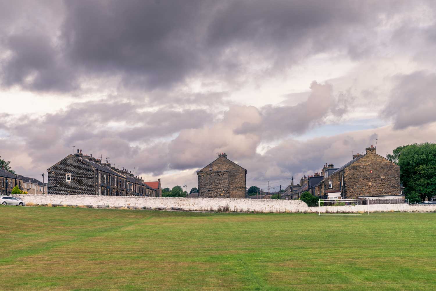 a large green field with buildings and a cloudy sky