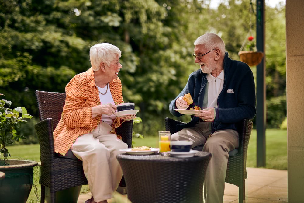 An older couple sitting enjoying breakfast on their terrace