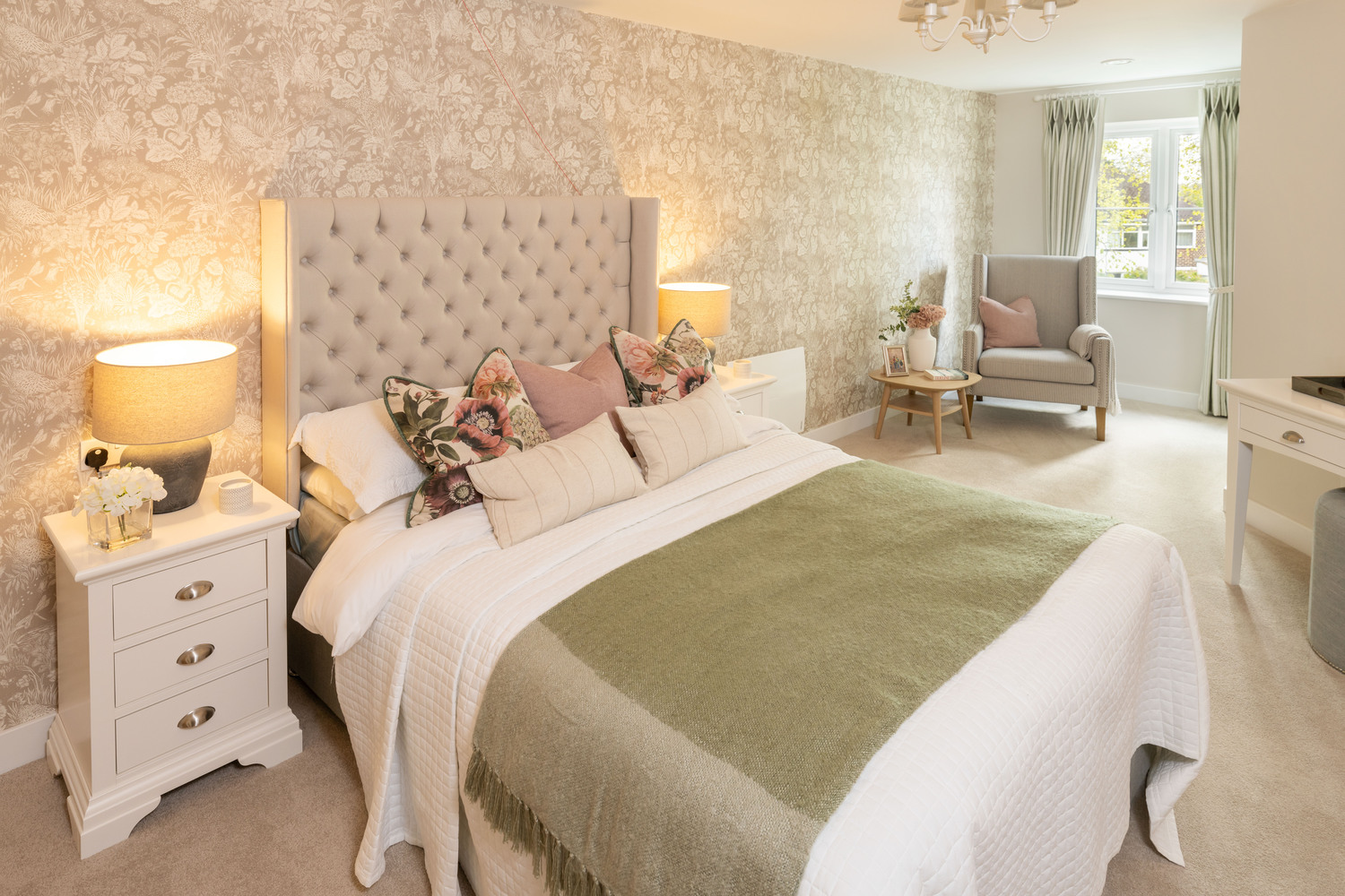 A beautifully made bed in a McCarthy Stone retirement apartment, featuring a plush sage throw and cushions.