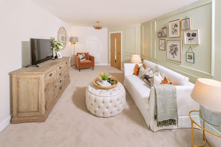 The inside of an apartment at a retirement living community. The living room features a large sofa and footstool. 