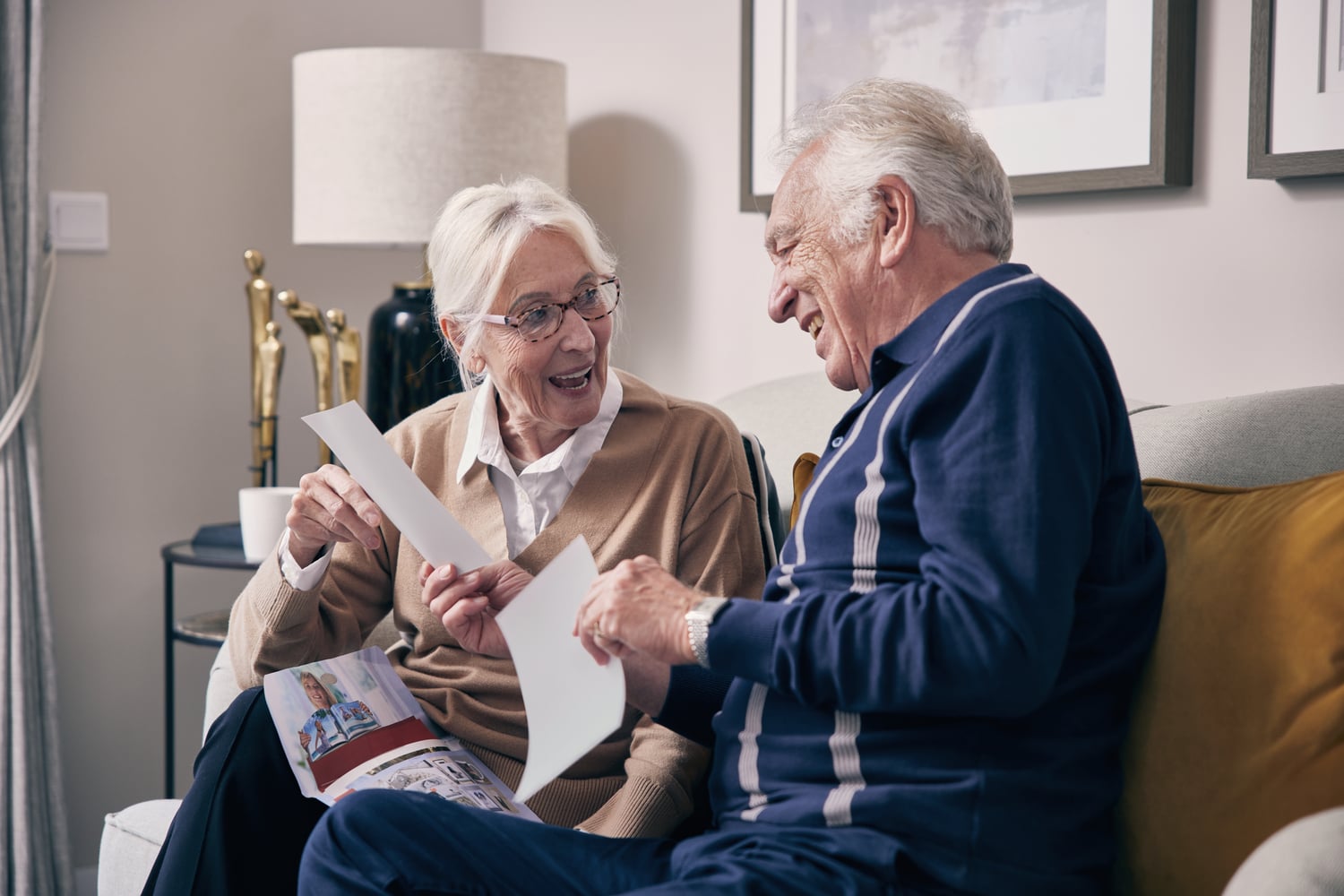 Retired couple on sofa looking at family photographs in their home.