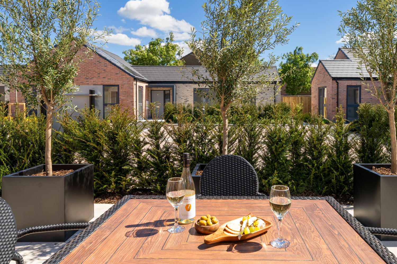 Wine and olives set on a table in a retirement bungalow’s private patio overlooking other neighbours.