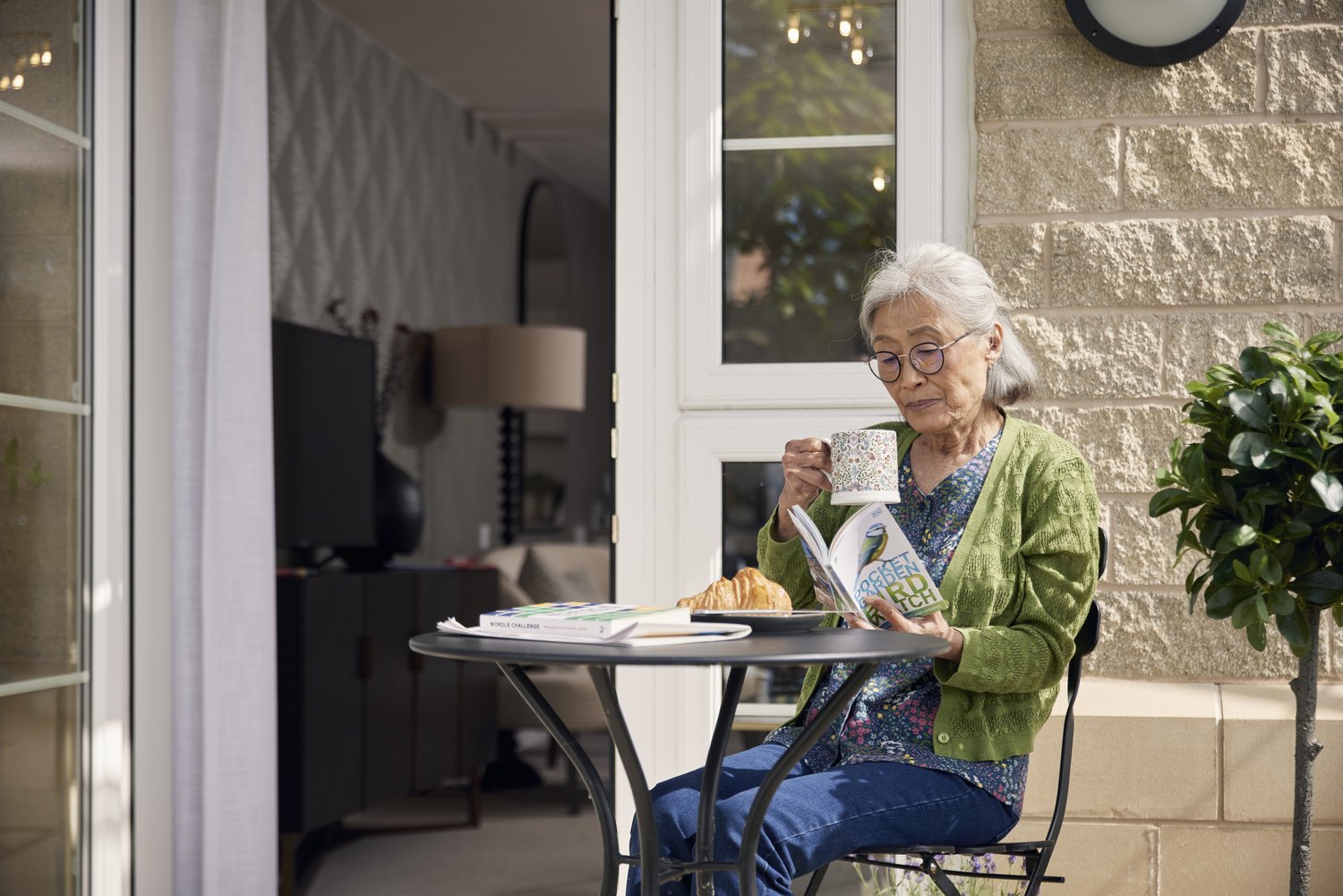 A senior resident sat at a table, reading outside her beautiful retirement housing which is exclusively available for those aged 60.