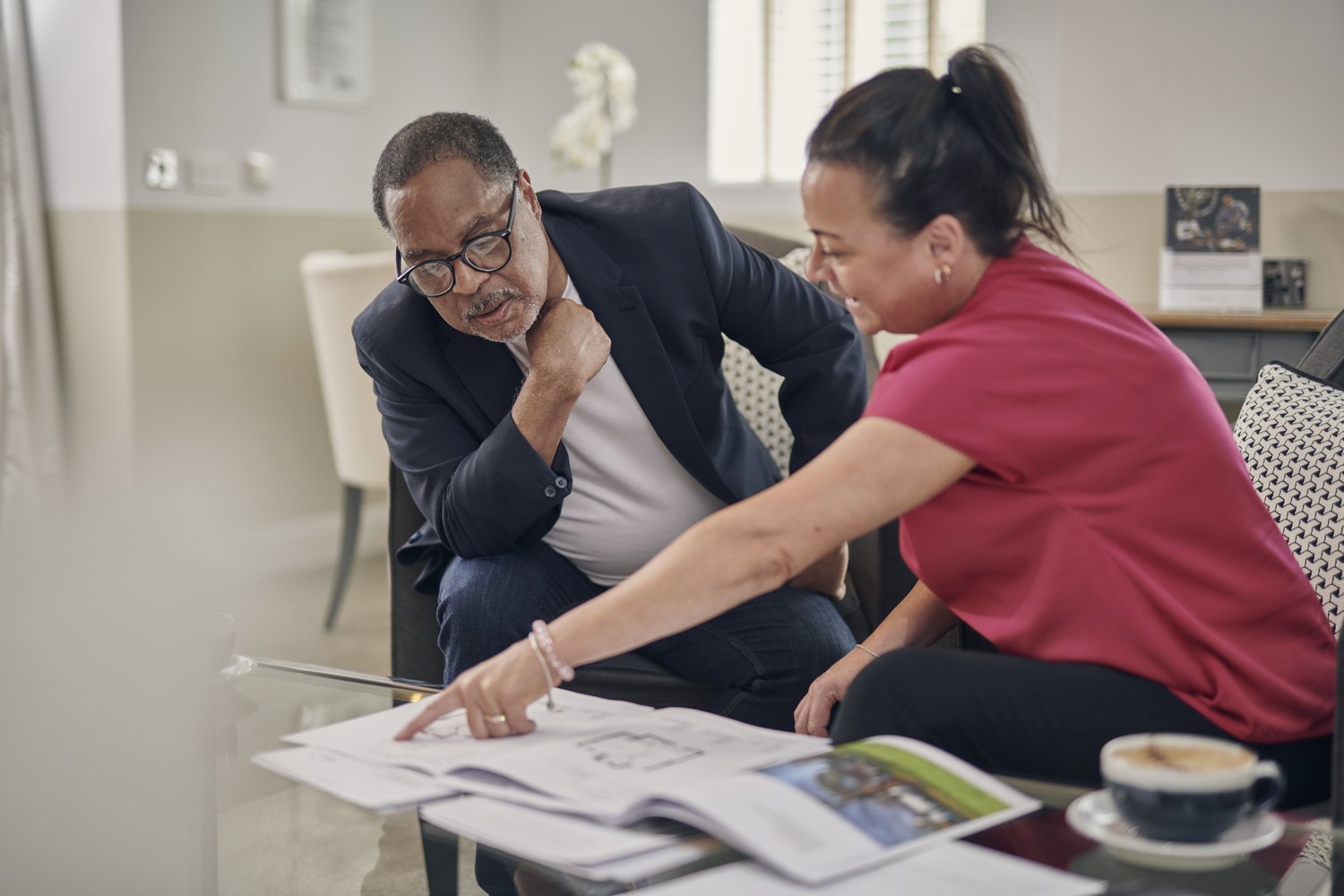 A senior person sat at a table, conversing with a friendly team member at a McCarthy Stone development.