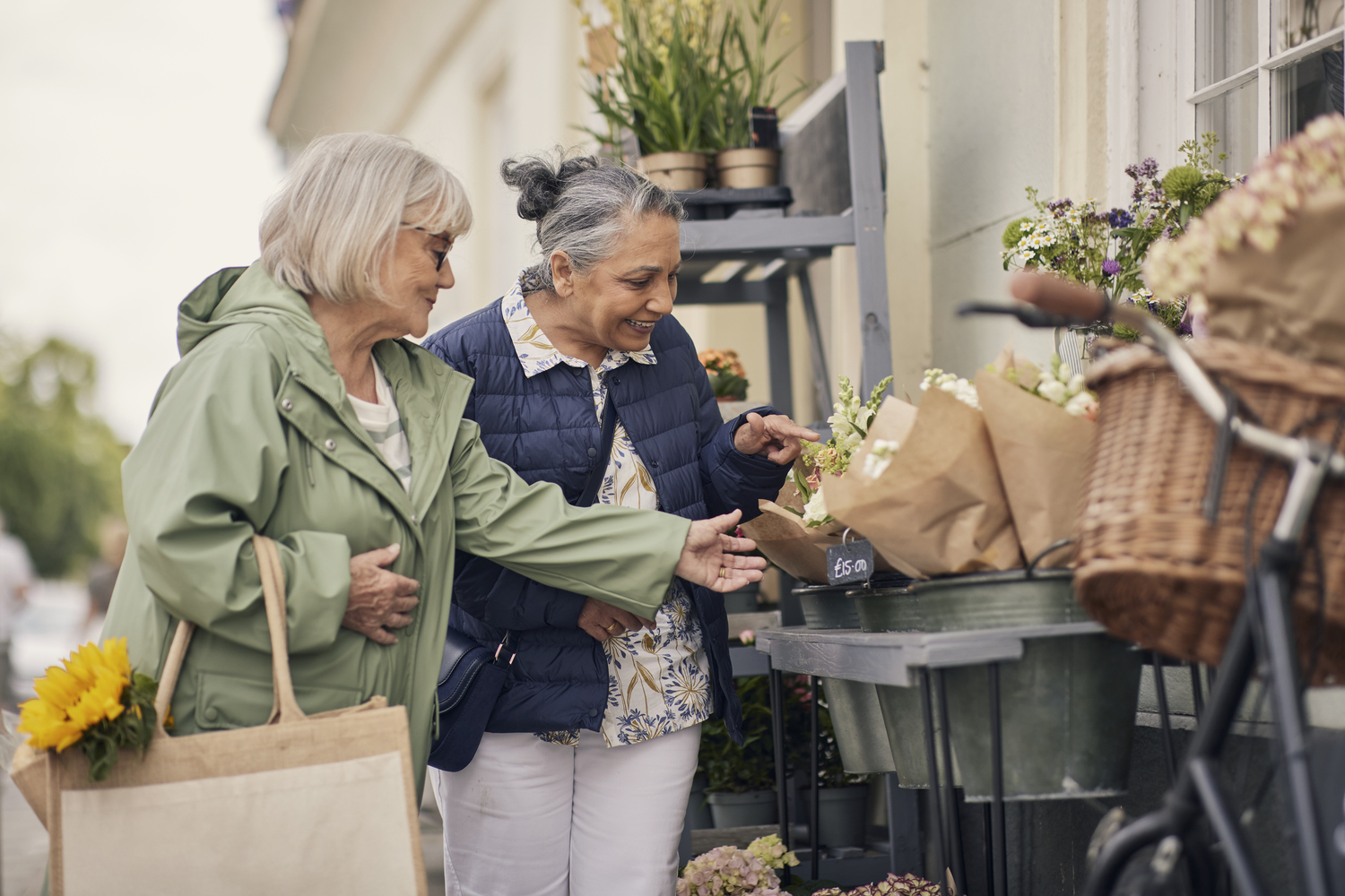 Two older women looking at flowers outside a flower shop in a retirement community setting.