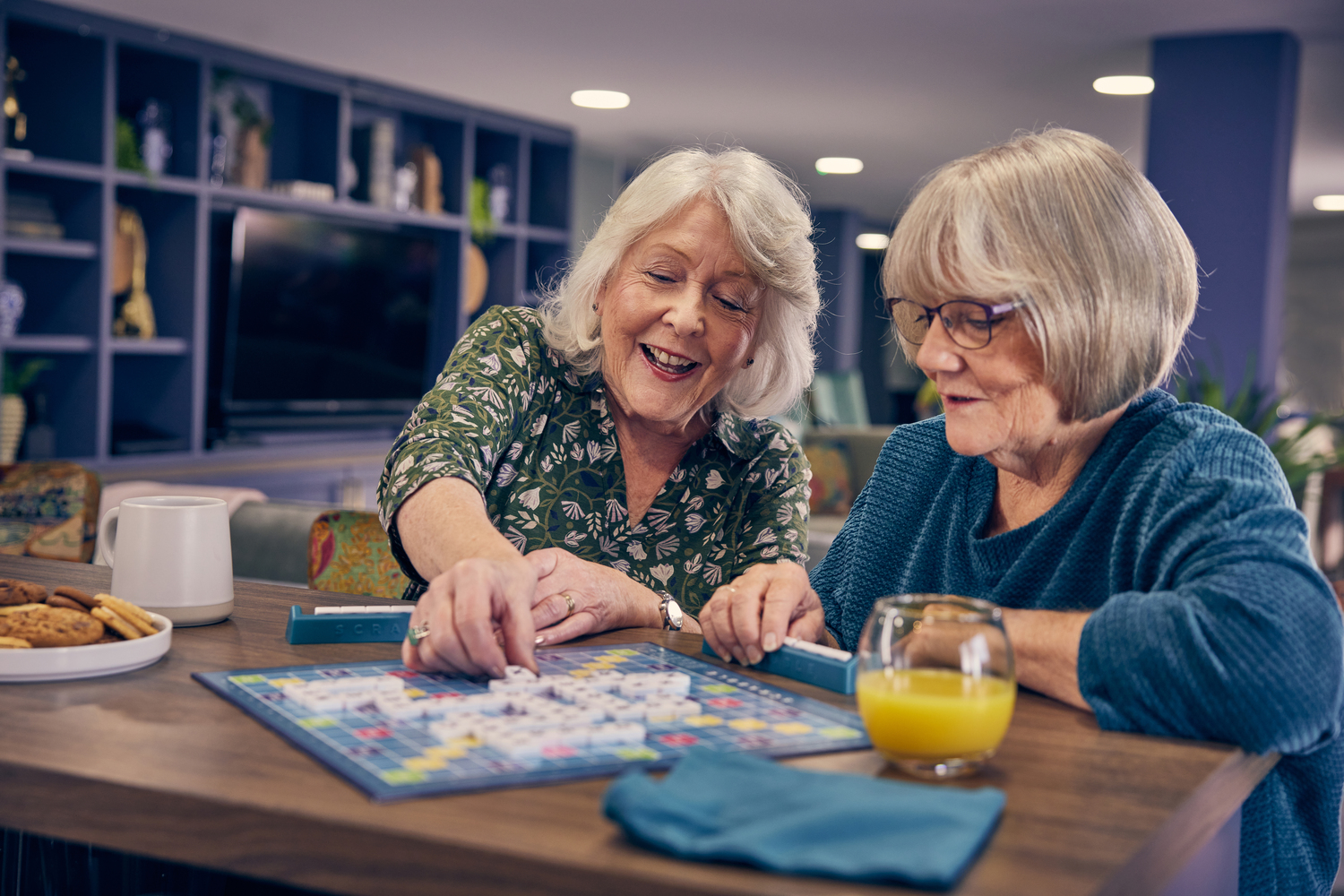 Two women playing scrabble in a supported living communal lounge.