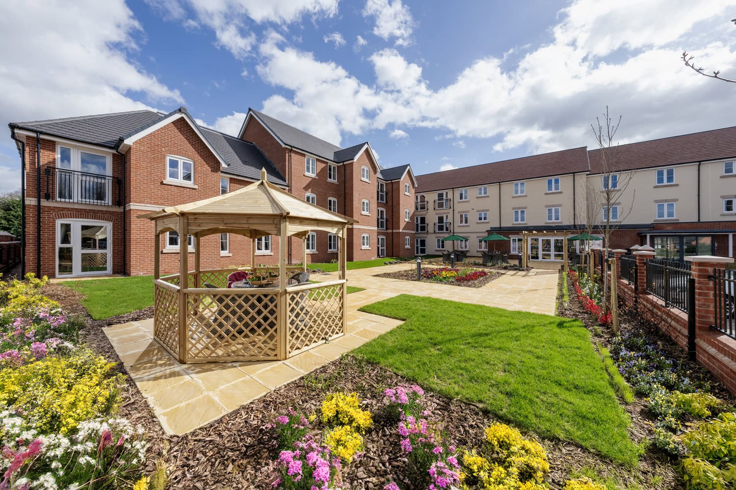 The exterior of a McCarthy Stone retirement community, featuring a large garden overlooked by apartment buildings