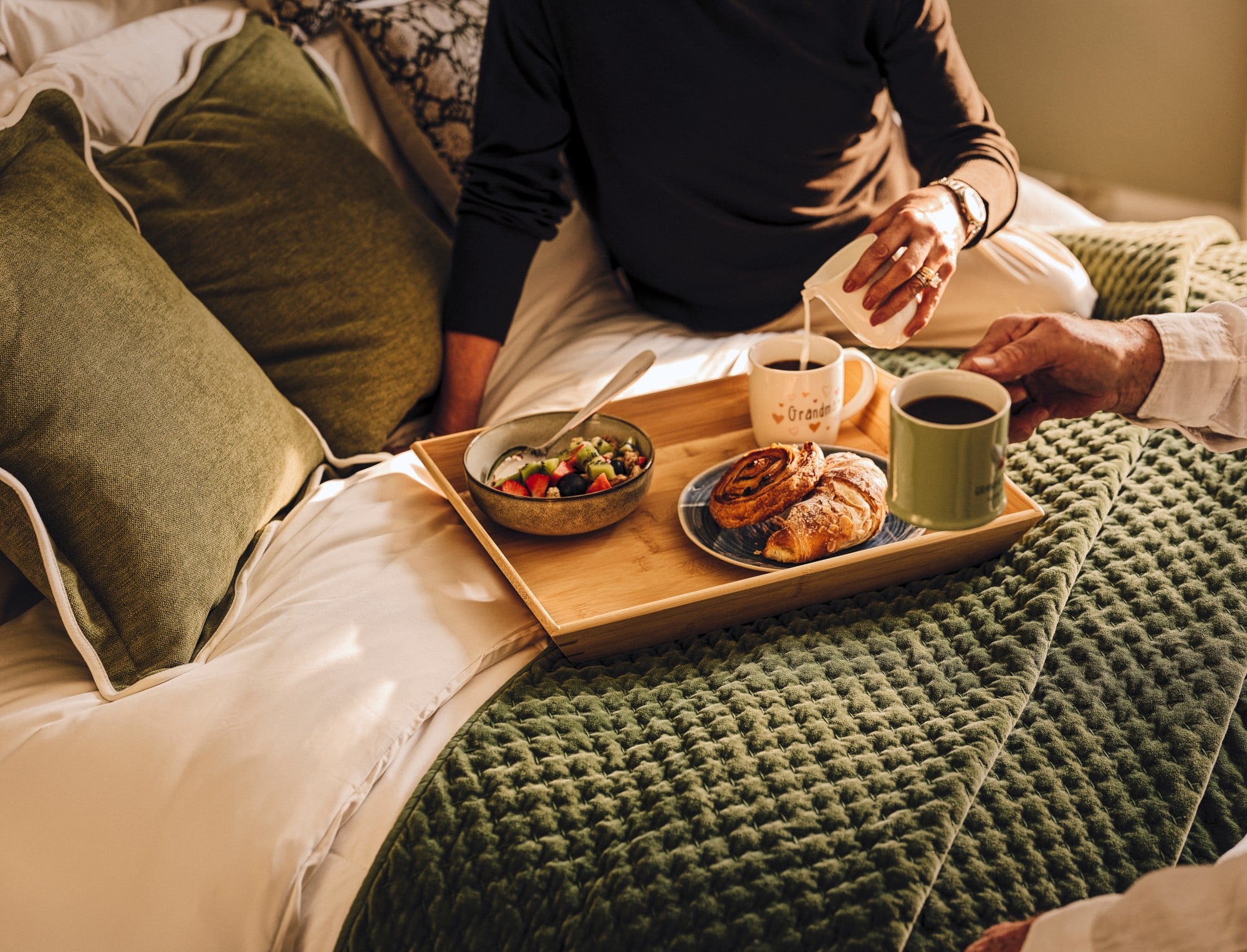 a person sitting on a bed with a plate of food and a cup of coffee