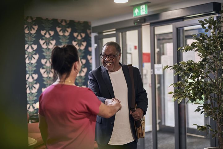 A retiree smiling and shaking hands with a member of staff in the reception of a McCarthy Stone independent living development
