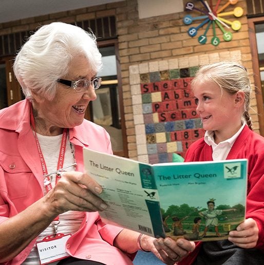 A retiree and child, holding the same book and smiling at one another.