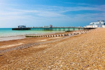 A pebbly beach and sea front in the foreground with Worthing Pier in the distance